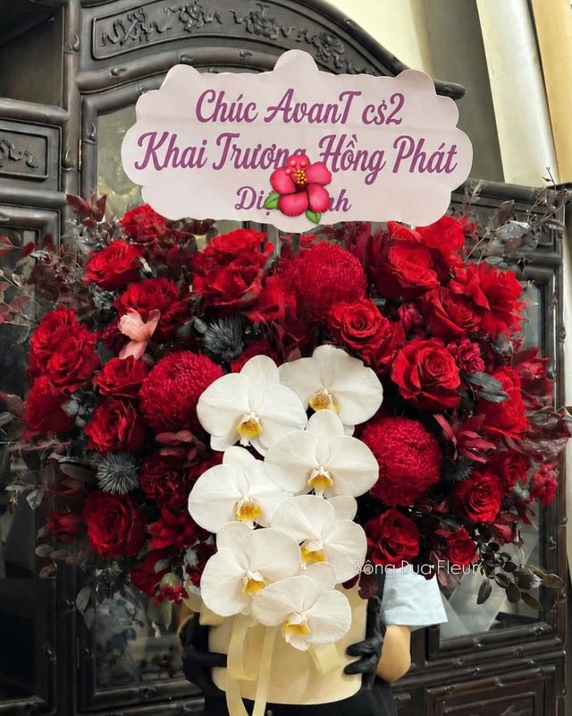 Kệ hoa khai trương tông đỏ với dải lan hồ điệp trắng và bảng chúc mừng.